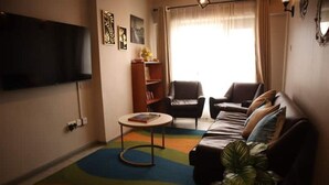 Una sala de estar con un sofá, sillones, una mesa de centro, una estantería y un televisor de pantalla plana montado en la pared.
