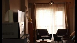 Una sala de estar con un sofá, dos sillones, una mesa de centro, un televisor y una zona de cocina con estufa.