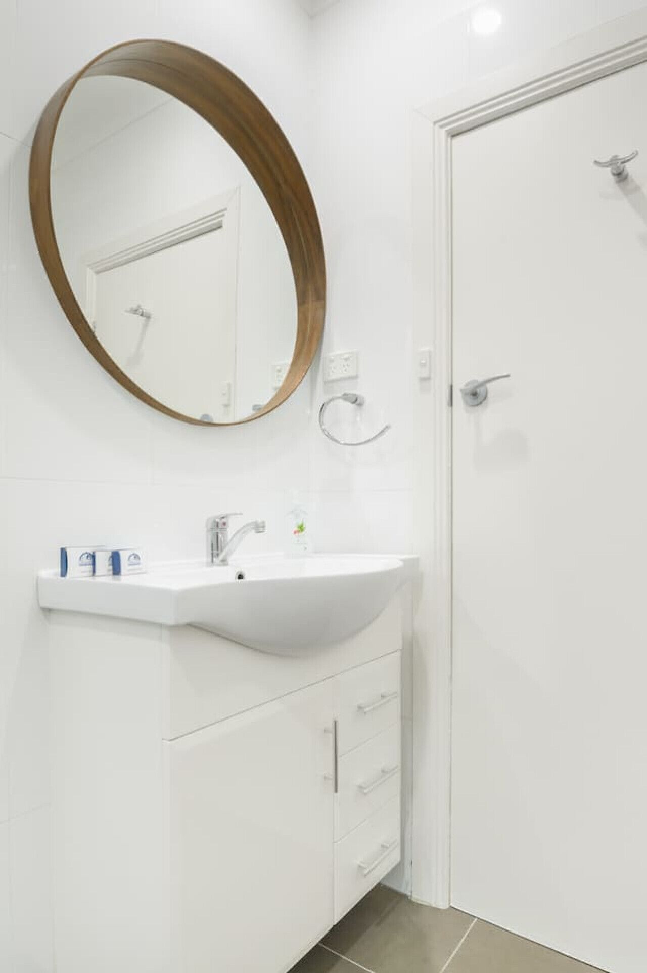 A bathroom with a white sink, a round mirror with a wooden frame, and a white door.