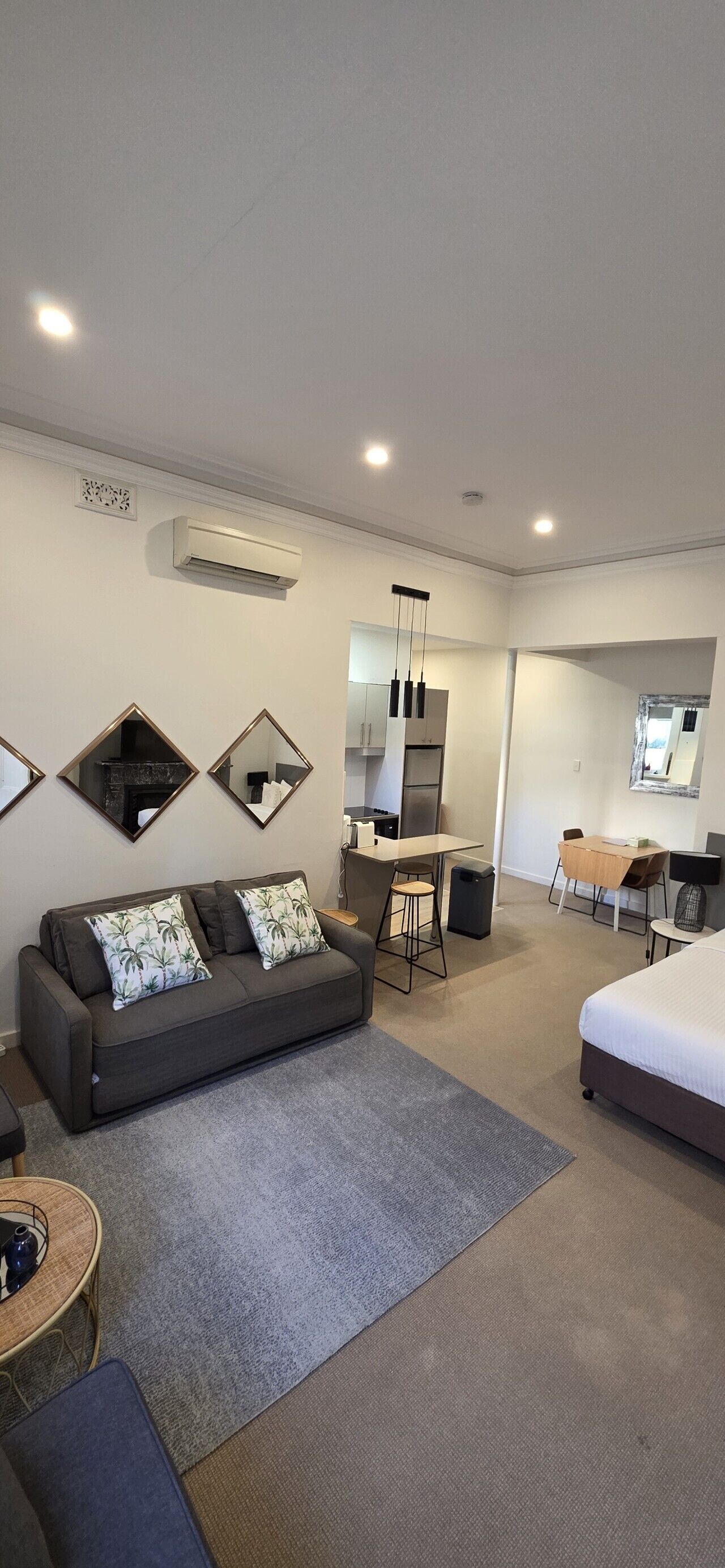 A modern hotel room with a sofa, a bed, a desk, and a dining area.