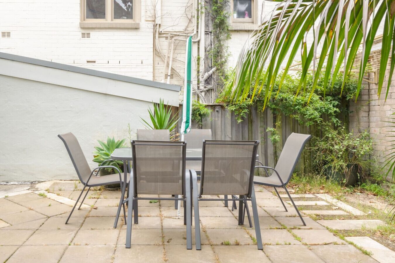 A patio with a table and chairs, surrounded by plants and a fence.