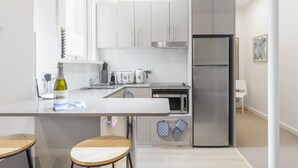 A modern kitchen with white cabinets, a stainless steel refrigerator, a sink, and a countertop with a bottle of wine. There are two stools at the counter. - Huge Designer Studio Next to Lovely Park (North Sydney)