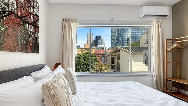 Habitación de hotel con una cama grande, vistas a la ciudad y cortinas en la ventana.