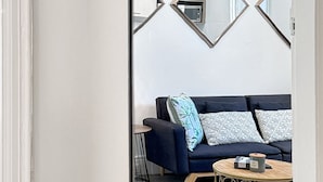Una sala moderna con un sofá azul oscuro, cojines estampados, una mesita auxiliar y una mesa de centro redonda con base trenzada.