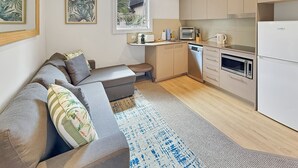 A modern kitchen with a built-in oven, microwave, and toaster. There is a gray sofa with cushions and a small table with a coffee machine. - Parkside 1 bedroom home, Whisper quiet (North Sydney)