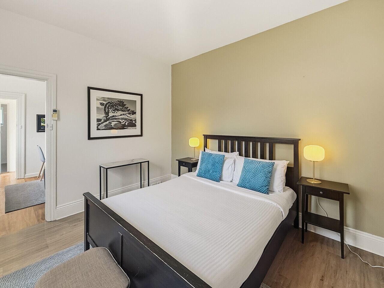 A bedroom with a bed, bedside tables, a nightstand, a lamp, and a framed picture on the wall.