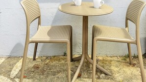 A small outdoor seating area with two chairs and a table, positioned against a white wall with a window above.