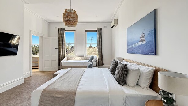 A hotel room with a large bed, a television, a painting, and a view of the outside.