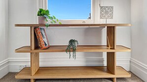A wooden multi-tiered shelf unit with a plant and a book on the top shelf.
