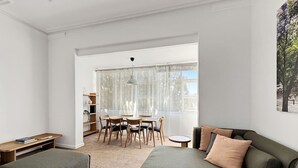 A modern living room with a sofa, ottoman, and a dining area with chairs and a table.
