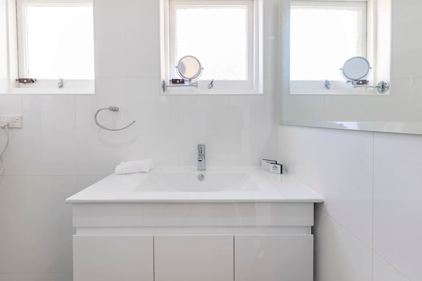 Uma casa de banho moderna com uma pia branca, dois espelhos e uma toalha.