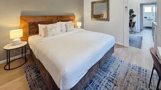 A bedroom with a large bed, a nightstand, a lamp, a mirror, and a view of the bathroom. - Cute 1 bedroom with private courtyard garden (North Sydney)