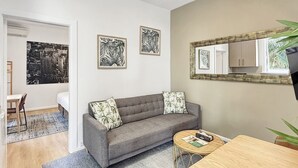 A modern living room with a grey sofa, a round coffee table, and a dining table. There are framed artworks on the walls and a large mirror above the sofa. - Cute 1 bedroom with private courtyard garden (North Sydney)