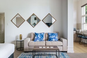 Un salon moderne avec un canapé beige, deux coussins bleus à motifs, une table basse et trois miroirs fixés au mur.