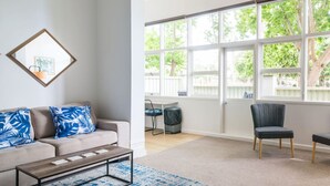 A living room with a large window, a sofa with patterned cushions, a coffee table, and a chair. - Sun Drenched Ground Floor Studio with Patio (North Sydney)
