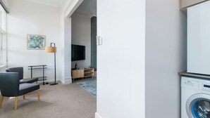 A modern living room with a grey sofa, a TV, a lamp, and a washing machine. - Sun Drenched Ground Floor Studio with Patio (North Sydney)