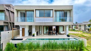 Una casa moderna de dos pisos con piscina, ventanas grandes y un patio.