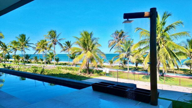 Zona de piscina con vista al océano y palmeras.