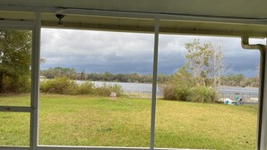 A room with a view of a grassy area and a body of water, with a white ceiling and a security camera. - Charming 2-bedroom, 1-bath lakefront house in the Ocala National Forest (Silver Springs)