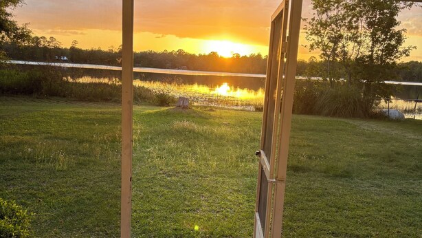 A view from inside a building looking out to a grassy area with a body of water and trees in the distance. - Charming 2-bedroom, 1-bath lakefront house in the Ocala National Forest (Silver Springs)