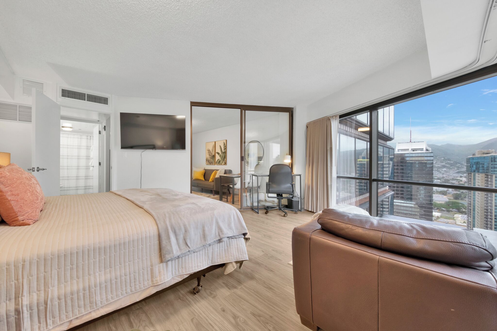 Une chambre d’hôtel moderne dotée d’un grand lit, d’un bureau avec une chaise, d’un téléviseur fixé au mur et d’une grande fenêtre donnant sur la ville.