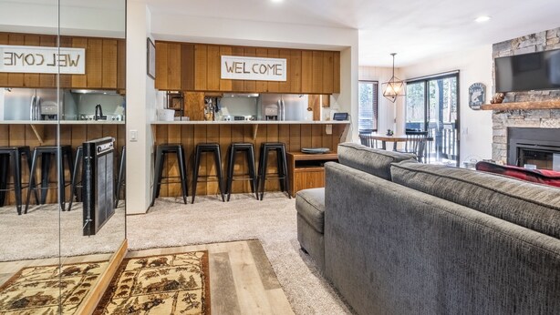 A modern living space with a kitchen, bar stools, a sofa, and a fireplace.
