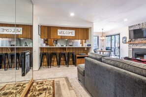 A modern living space with a kitchen, bar stools, a sofa, and a fireplace.