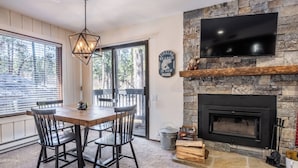A dining area with a wooden table and chairs, a stone fireplace, a television mounted on the wall, and a sign indicating the fishing season is open.