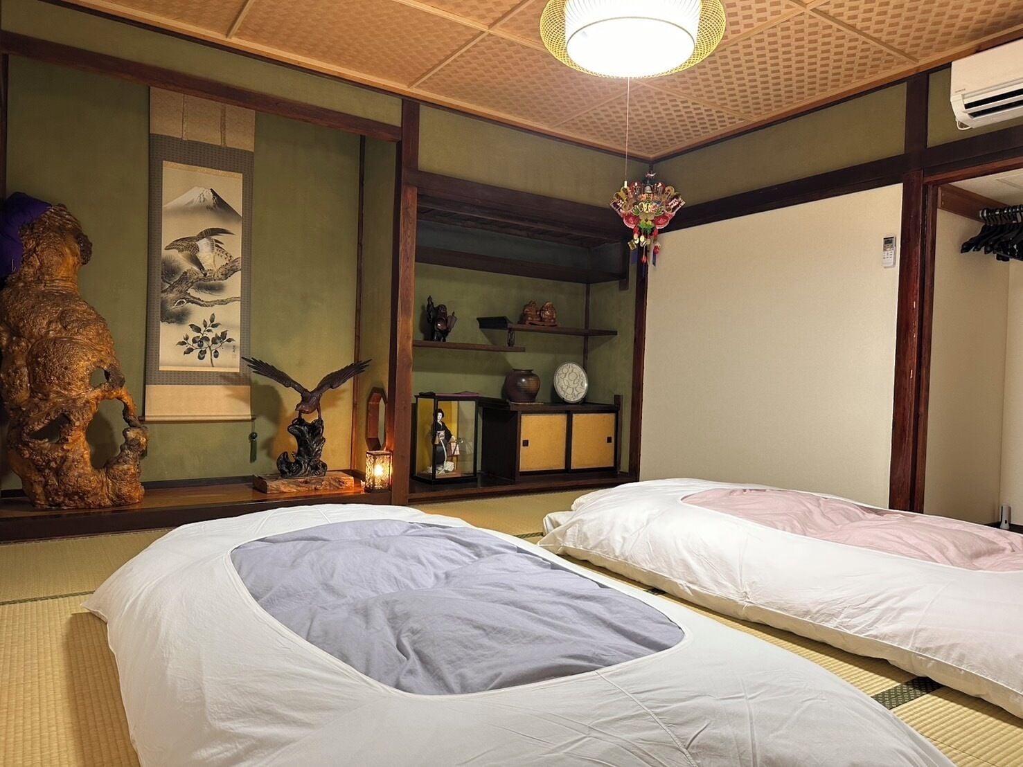 A traditional Japanese room with tatami mats, a shoji screen, a wooden statue, and a hanging decorative piece.