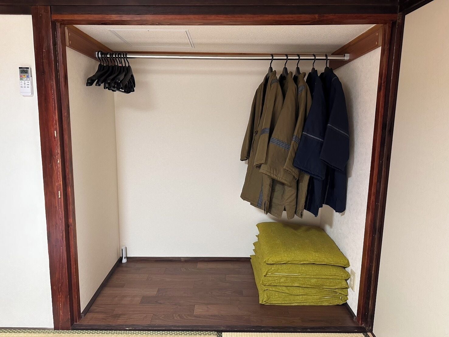 Un vestidor con piso de madera, una barra para colgar chaquetas y una pila de ropa doblada.