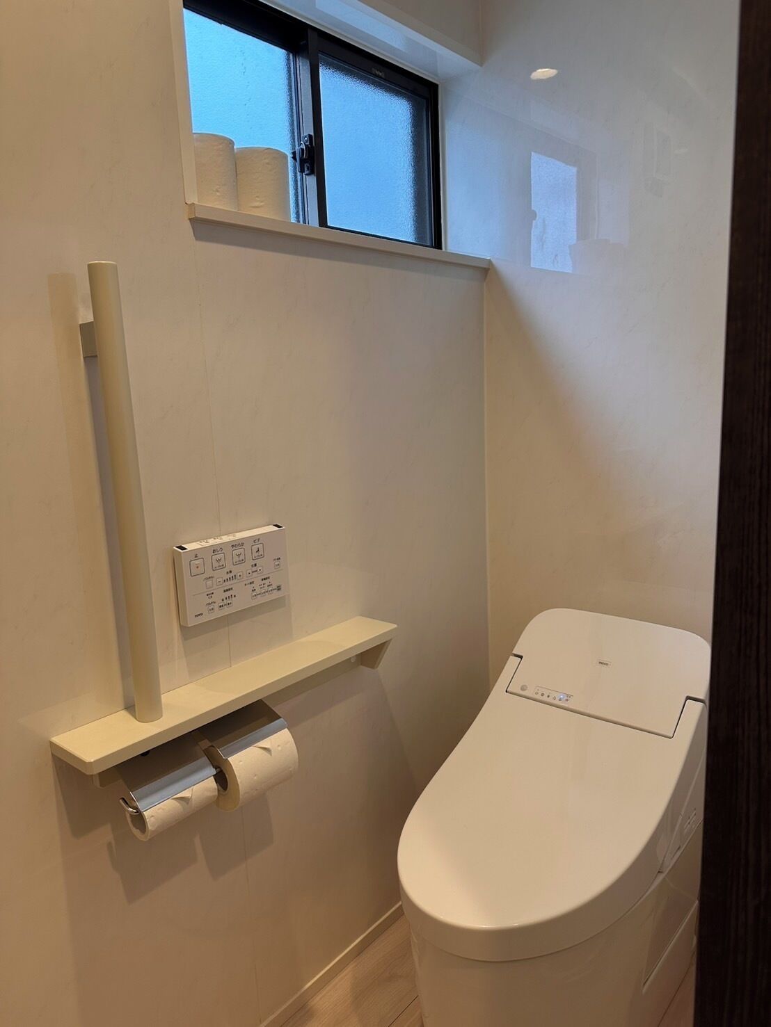 A modern bathroom with a toilet, a toilet paper holder, and a shelf with toilet paper.