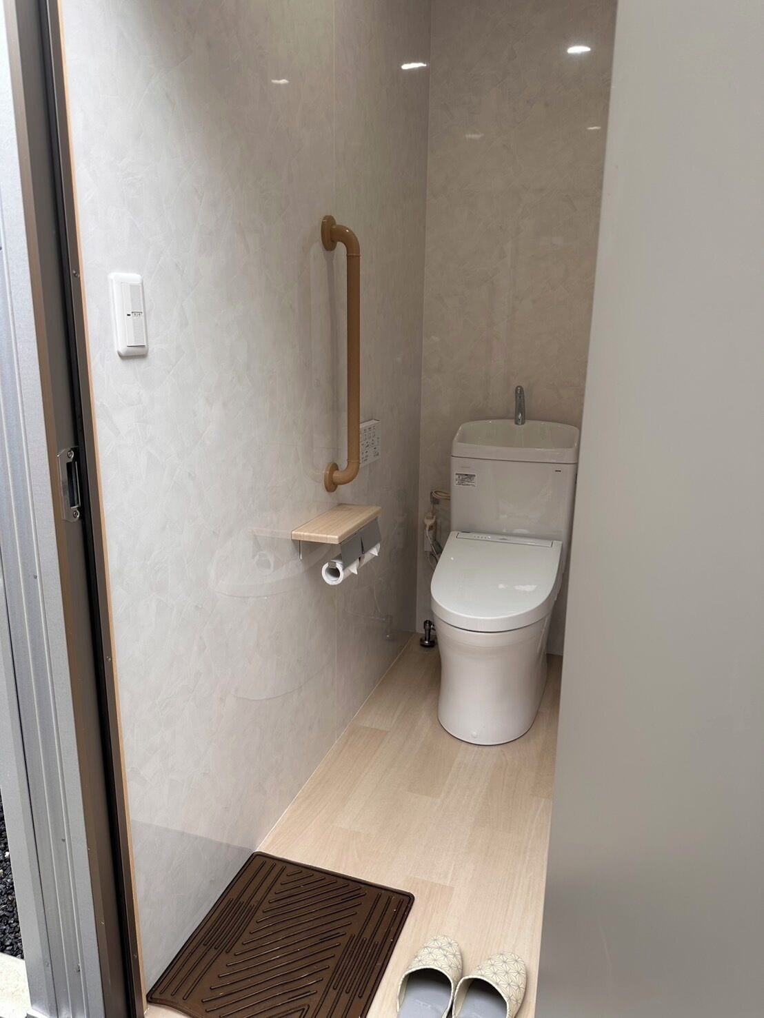 Un baño pequeño con inodoro, barra de apoyo y un estante.