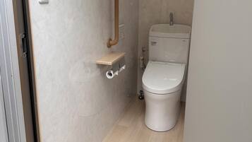 Un baño pequeño con inodoro, barra de apoyo y un estante.