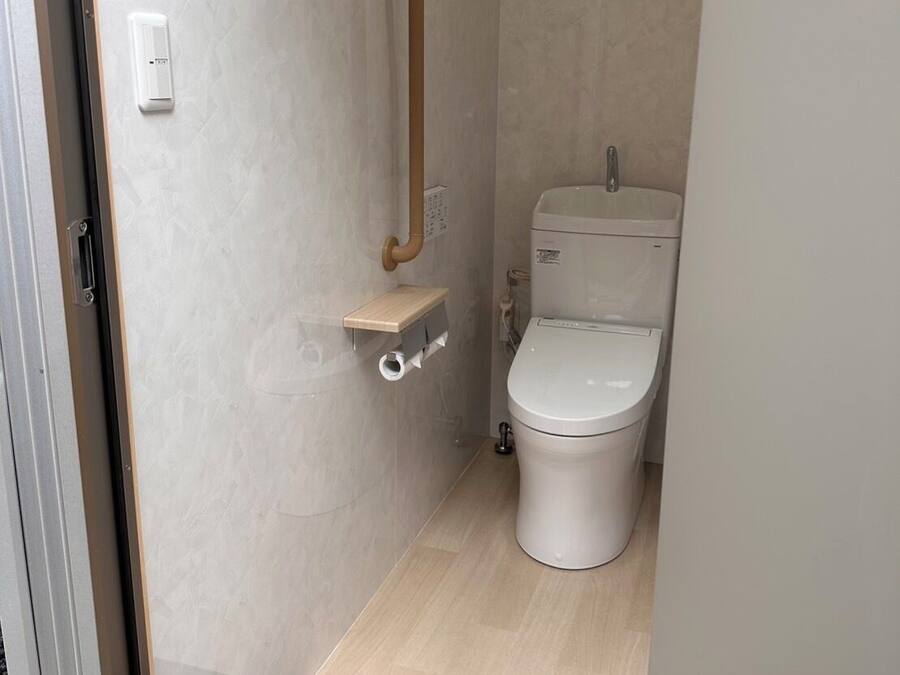 Un baño pequeño con inodoro, barra de apoyo y un estante.