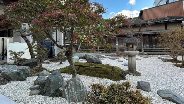 A traditional Japanese garden with a rock arrangement, a moss-covered stone, and a small tree with pink flowers. - Warouan (Nikko)