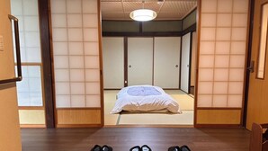 A traditional Japanese room with tatami flooring, a bed with white bedding, and a sliding door. - Warouan (Nikko)