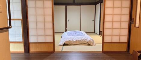A traditional Japanese room with tatami flooring, a bed with white bedding, and a sliding door.