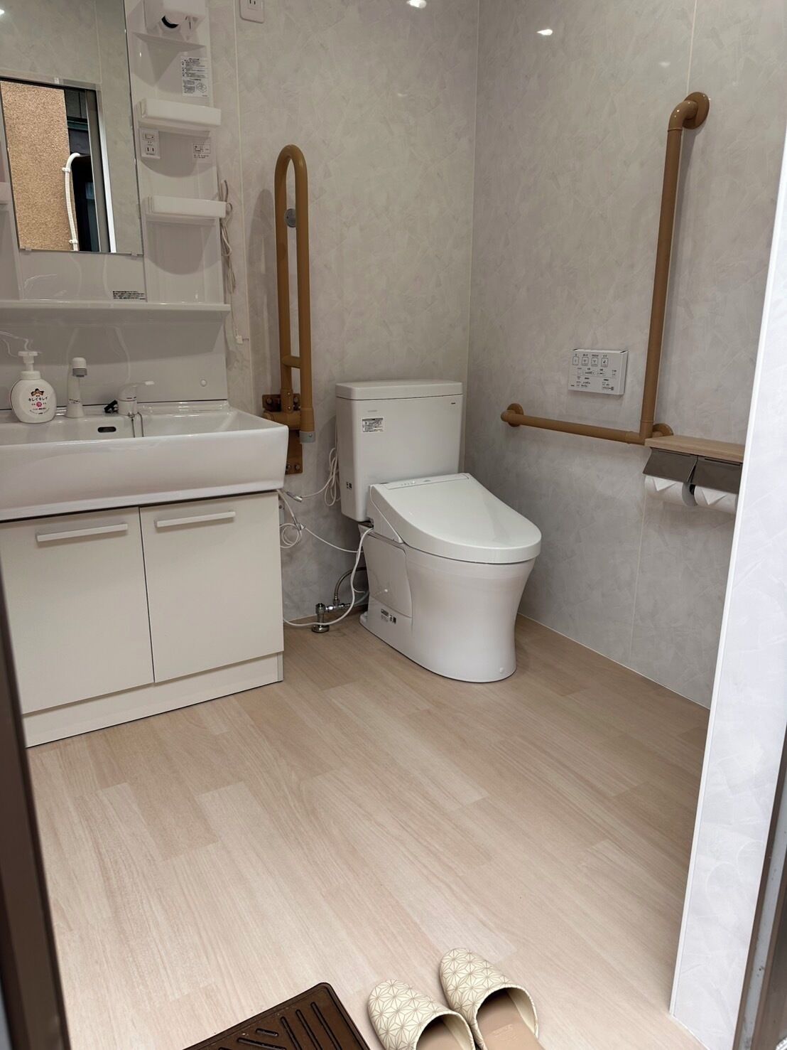 A modern bathroom with a toilet, sink, and mirror. There is a wooden handrail and a towel rack on the wall.