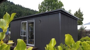 A modern building with a large glass door, surrounded by greenery and a view of a forested area. - Custom Cabin -  In Town - Hot Tub - Super King Bed (Queenstown)