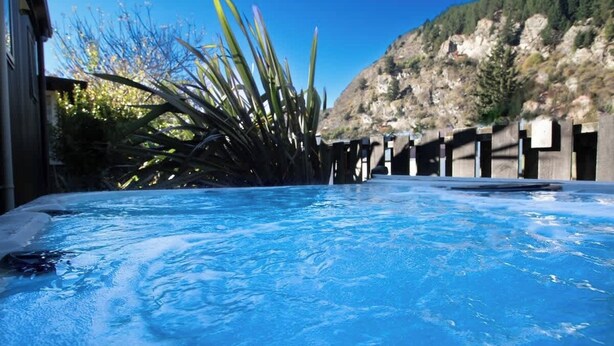 A hot tub with a clear view of the surrounding area, including a mountain and some vegetation. - Custom Cabin -  In Town - Hot Tub - Super King Bed (Queenstown)