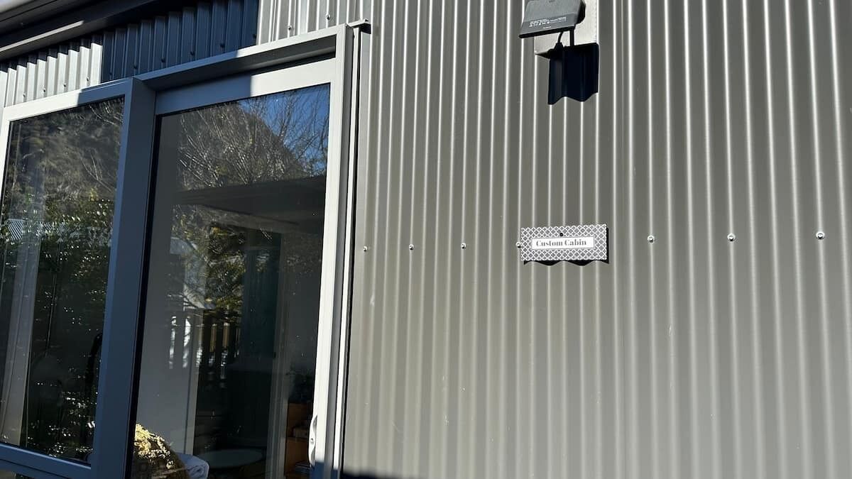 A metal building with a sliding glass door, a sign reading 'Custom Cabin,' and a small black object on the wall.