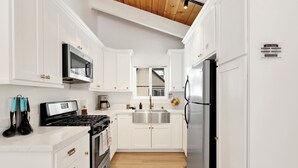 Una cocina moderna con armarios blancos, electrodomésticos de acero inoxidable y techo de madera.