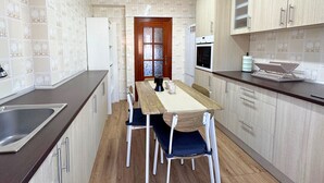 Una cocina compacta con una mesa y sillas de madera, un refrigerador, un horno y armarios de color claro.
