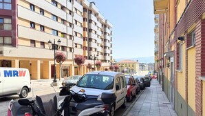 Una calle bordeada de coches aparcados y una hilera de edificios de varios pisos con balcones.