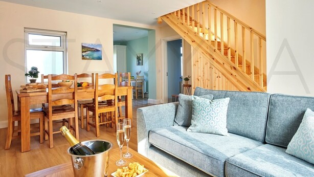 A modern living room with a wooden dining table, a grey sofa, and a staircase. - Shepherds Rest - Four bedroom home (County Kerry)