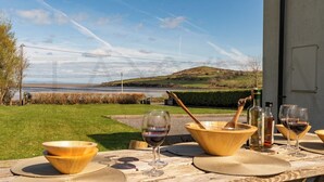 A table set outdoors with a view of a coastal landscape, including a body of water and hills. - Owenmore Lodge 3 bedroom home (County Kerry)