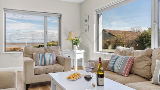 A modern living room with two beige sofas, a white coffee table, and a view of the countryside through large windows. - Owenmore Lodge 3 bedroom home (County Kerry)