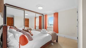 A hotel room with a large bed, two bedside tables, a mirror, and a window with orange curtains.