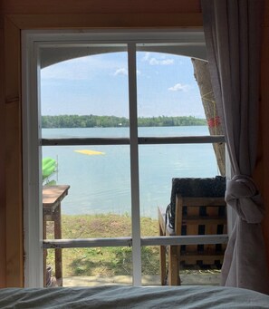 Una habitación con un amplio ventanal con vistas a un lago, una terraza de madera y una silla atada al marco de la ventana.