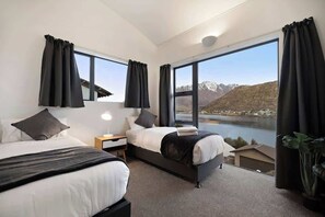 A modern hotel room with two beds, large windows, a view of mountains and a lake, and a potted plant. - Peak Paradise Lodge - Hot Tub - Lake Views (Queenstown)